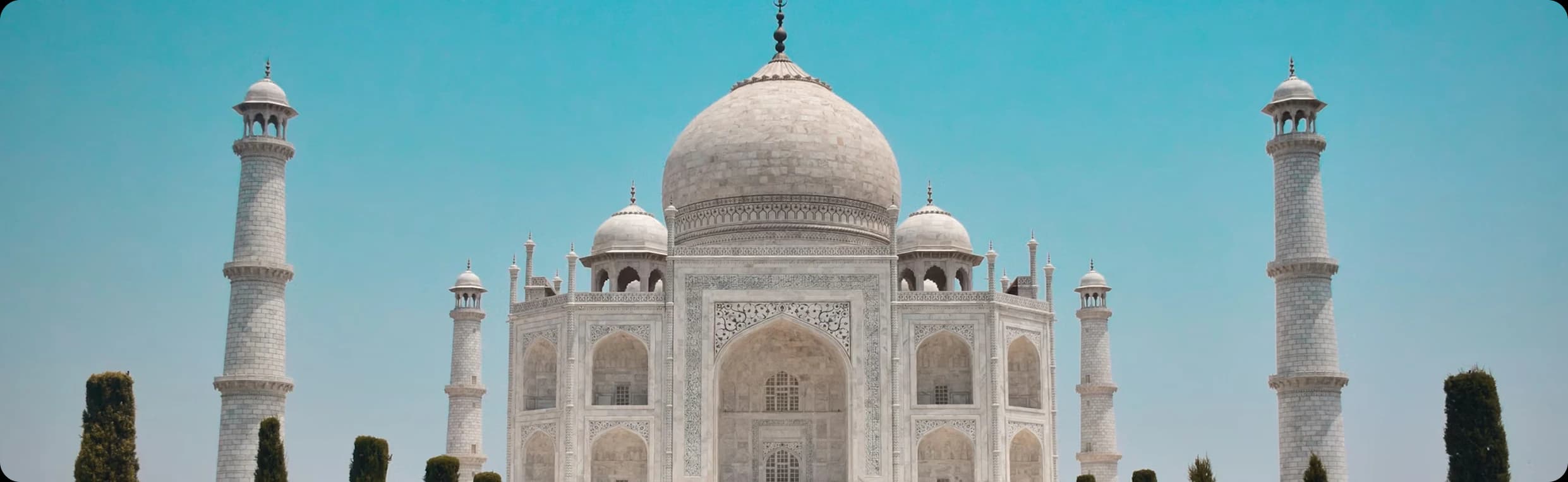 Front view of Taj Mahal white marble mausoleum with minarets and cypress trees against clear blue sky in Agra India
